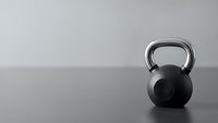 Black kettlebell on wooden floor against gray wall in minimalist gym setting for fitness training and strength workout routines.