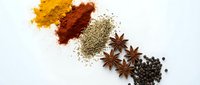 Colorful aromatic spices including turmeric, paprika, oregano, star anise and black peppercorns arranged on white background for culinary cooking.