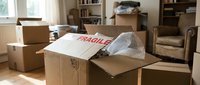 Moving day chaos with fragile cardboard boxes scattered across living room floor ready for relocation and unpacking in new home.