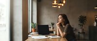Young professional woman working on laptop in modern office space with warm lighting and plants creating productive workspace atmosphere.