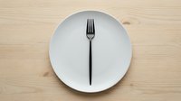 Empty white plate with black fork on wooden table surface, minimalist dining and food service concept.