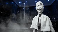 Skeletal figure wrapped in white cloth and towel standing in steamy bathroom with modern fixtures and blue lighting, suitable for horror, Halloween, and surreal design projects.