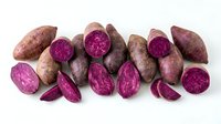 Purple sweet potatoes whole and sliced showing vibrant magenta flesh on white background. Organic root vegetables for healthy cooking and nutrition.