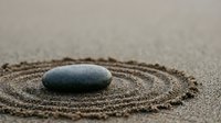 Zen stone placed in center of circular sand pattern creating peaceful meditation garden scene for mindfulness and relaxation practices.