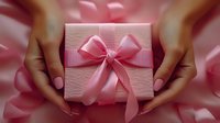 Female hands holding pink gift box with elegant satin bow against soft pink background, romantic holiday present packaging for special occasions.
