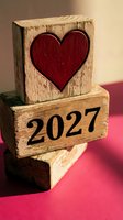 Wooden blocks stacked with red heart symbol and 2027 date on pink surface, representing love, romance, and future planning for Valentine's Day or anniversary celebrations.