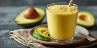 Creamy avocado smoothie in glass with fresh avocado slices on rustic background, healthy breakfast or nutritious snack option.