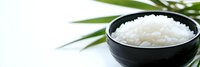 Steamed white jasmine rice in black ceramic bowl with green palm leaves against white background, food photography for restaurant menu.