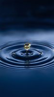 Golden water droplet creating ripples on calm blue surface with dramatic lighting and reflections for nature and purity concepts.