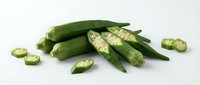 Fresh green okra pods whole and sliced showing seeds inside on white background. Healthy organic vegetable ingredient for cooking and nutrition.