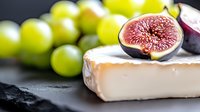 Fresh ripe fig cut in half on top of soft brie cheese with green grapes in background on dark slate surface, macro food photography for gourmet menu.