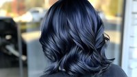 Metallic blue-black hair color with dimensional highlights and waves styled in modern layered cut, photographed from behind showing luxurious shine and movement.