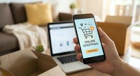 Online shopping app on smartphone screen with shopping cart icon and checkout button, person browsing e-commerce website on laptop in cozy living room.