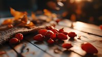 Fresh red rosehips scattered on rustic wooden surface with burlap fabric in warm autumn sunlight, creating cozy seasonal atmosphere.