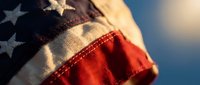 Weathered American flag waving against blue sky, close-up of stars and stripes fabric texture, patriotic symbol of freedom and national pride.