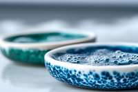 Artistic ceramic bowls with vibrant turquoise and blue crystalline glaze patterns showcase handcrafted pottery detail in shallow depth of field macro photography.