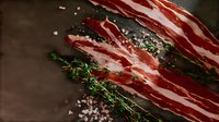 Raw bacon strips with fresh thyme sprigs and pink salt crystals on dark rustic background, dramatic food photography highlighting meat texture and seasoning.