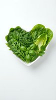 Fresh mixed green leafy vegetables including spinach, lettuce, and broccoli arranged in heart shape on white plate for healthy eating, nutrition, and diet concepts.