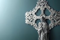 Religious silver ornate cross with Virgin Mary figure against teal background, shallow depth of field creating atmospheric spiritual composition.