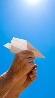 Hand holding white paper airplane against bright blue sky background ready to launch into flight for freedom and adventure concepts.