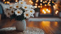 Fresh white daisies in textured ceramic vase on crochet doily, warm bokeh lights creating cozy atmosphere, romantic home decor on wooden table surface.