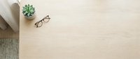 Flat lay workspace with eyeglasses, succulent plant, and gray fabric on light wooden desk surface, suitable for business and lifestyle design projects.