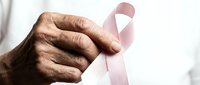 Elderly hands holding pink ribbon symbol for breast cancer awareness campaign and women health support advocacy.
