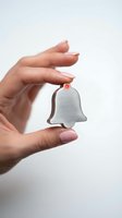 Woman's hand with pink manicure holding a small metallic bell-shaped icon with a red notification dot on white background.