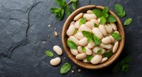 White lima beans in wooden bowl with fresh mint leaves on dark slate background for healthy cooking and nutrition concepts.