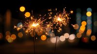 Glowing sparklers burning against dark background with festive bokeh lights, creating magical holiday atmosphere for celebration designs.
