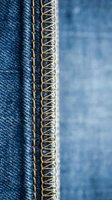 Close-up macro shot of denim fabric seam with golden yellow decorative stitching thread detail on blue jeans material for fashion and textile design projects.