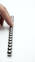 Hand touching a row of shiny chrome steel magnetic balls aligned on white surface, demonstrating magnetism and precision in science or physics concepts.