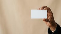 Male hand holding blank white business card against neutral beige background, suitable for corporate branding, marketing mockups, and professional presentations.