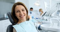 Middle-aged Caucasian woman smiling in dental chair during checkup at modern clinic. Healthcare professional consultation and oral hygiene concept.