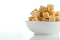 Brown sugar cubes in white ceramic bowl on clean background for cooking and baking projects.