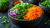 Fresh colorful vegetable salad bowl with lettuce, carrots, red onion and herbs on dark background for healthy eating and nutrition concepts.