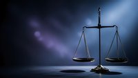 Scales of justice on dark blue background with dramatic lighting for legal concepts and law firm presentations.