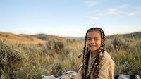 Young girl with braided hair smiling in golden grassland field during sunset, outdoor portrait for lifestyle and nature themes.