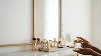Young woman with dark skin tone applying luxury cosmetics at vanity mirror with golden frame, showcasing makeup products and skincare routine for beauty and wellness content.