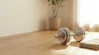 Metallic dumbbell on wooden table with plant and notebook in bright sunlight, fitness and wellness lifestyle setup for gym training.