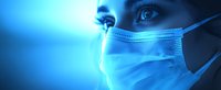 Close up view of medical professional wearing protective surgical face mask in dramatic blue lighting, emphasizing eyes and determined expression. Healthcare concept.