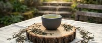Green tea in ceramic cup on wooden slice with loose tea leaves scattered around, outdoor garden setting with natural lighting for wellness and relaxation concepts.