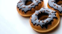 Freshly baked donuts with dark chocolate glaze and sprinkles on white background. Close-up view shows rich texture and glossy coating for food photography.
