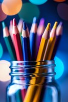 Colorful wooden pencils in glass jar against blue bokeh background, artistic macro photography with soft focus and vibrant colors for education concepts.