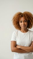 Young African American woman with curly hair in white t-shirt standing confidently with crossed arms against neutral background for lifestyle content.