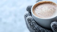 Steaming hot chocolate in white ceramic cup held by hands in cozy grey knitted mittens against winter background, creating warm and comforting atmosphere.