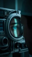 Futuristic astronaut in metallic suit with glowing cyan eye visible through helmet visor, surrounded by advanced technology and control panels in dark sci-fi environment for space exploration concepts.