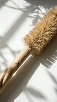 Natural coconut fiber cleaning brush with wooden handle in sunlight with plant shadows for eco-friendly household cleaning and sustainable living.
