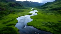 Meandering river flows through vibrant green valley with dramatic mountain peaks in background. Pristine wilderness landscape showcases nature's organic patterns.