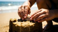 Woman hands building sandcastle on sunny beach with ocean waves in background during summer vacation leisure activity.